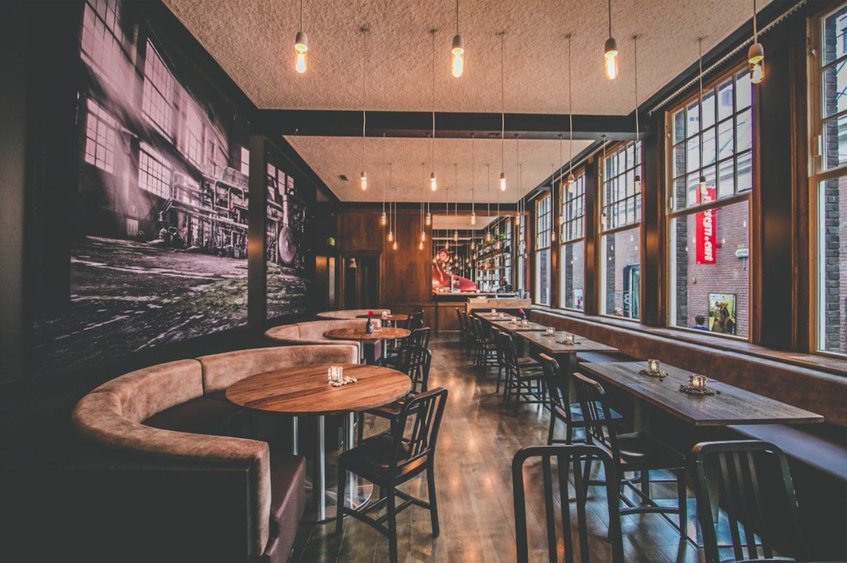Adapted Bierfabriek dining area with round tables, timber surfaces, pendant lights and a large wall image